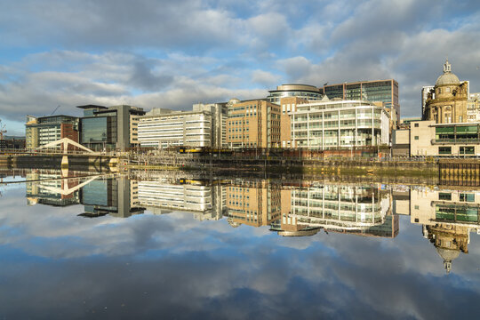 View of the Clyde River reflecting the buildings under a partly cloudy sky in the city, creating a mirrored urban landscape, Glasgow, Scotland, United Kingdom.