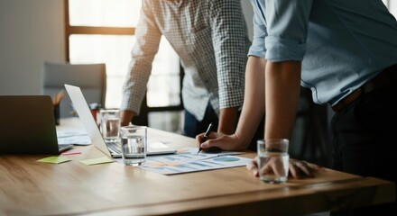 Business meeting with colleagues leaning over table reviewing charts and plans