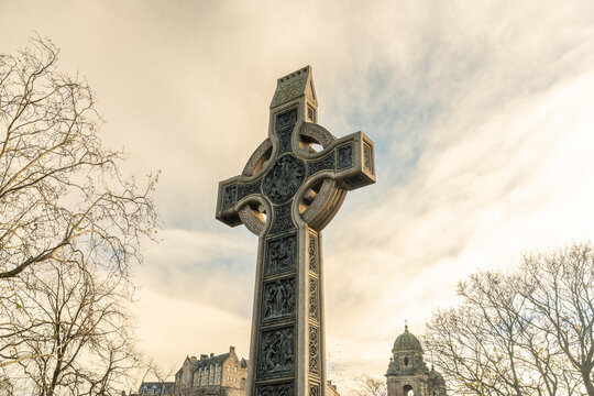 View of a towering Celtic cross, etched with intricate details, stands proud against a backdrop of a cloudy sky and distant buildings, Edinburgh, Scotland, United Kingdom.