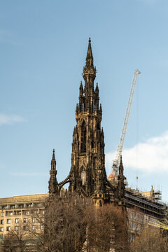 View of the towering, gothic spire of the Scott Monument piercing the crisp blue sky, juxtaposed with a modern crane, a dance of history and progress, Edinburgh, Scotland, United Kingdom.