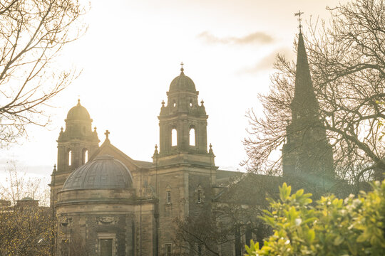 View of a golden sandstone tower of St John's Episcopal Church with Scottish flag fluttering atop, framed by the stark branches of winter trees, Edinburgh, Scotland, United Kingdom.