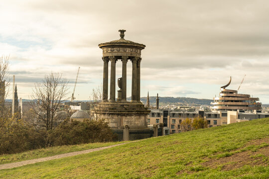 View of the weathered Dugald Stewart Monument stands proudly atop Calton Hill, overlooking the cityscape under a sky brushed with soft, diffused light, Edinburgh, Scotland, United Kingdom.