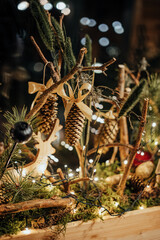 Close-up of golden pinecone ornament tied with a satin ribbon, surrounded by pine branches, twigs, and warm fairy lights in a festive arrangement