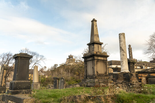 View of weathered tombstones and monuments stand solemn against a backdrop of rolling hills and cloudy skies in Old Calton cemetary, Edinburgh, Scotland, United Kingdom.