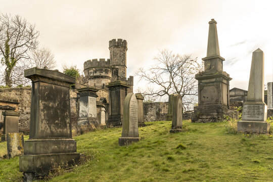 View of aged tombstones and monuments stand in solemn silence under a pastel sky, with the cylindrical tower in Old Calton, Edinburgh, Scotland, United Kingdom.