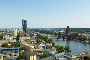 View of the Main River winding through a vibrant cityscape, reflecting the clear sky, with modern skyscrapers punctuating the skyline, Frankfurt am Main, Hessen, Germany.