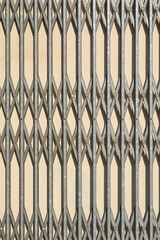 A close-up detail of a metal security grille with a diamond pattern in front of a light-colored wall