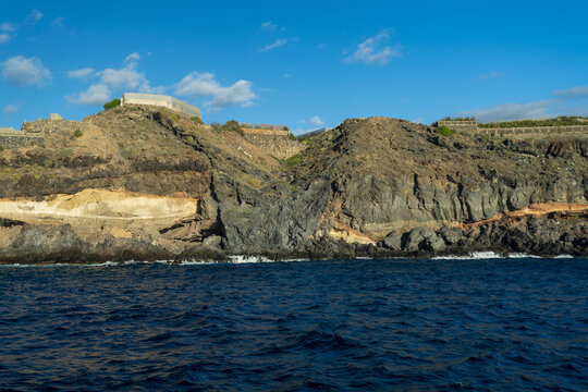 View of rugged cliffs rise majestically from the deep blue sea, their stratified layers painted in earth tones under a bright sky, Acantilados de Los Gigantes, Tenerife, Spain.