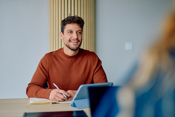 Man smiling at a business meeting, actively listening and writing in his notebook, showing...