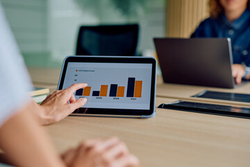 Professionals analyzing customer data charts on a tablet, planning business strategy in a modern office meeting