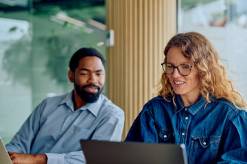 Diverse business colleagues working together on laptops, discussing project ideas and sharing information in a bright corporate office setting