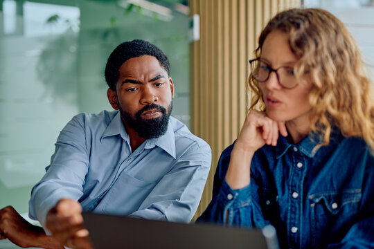 Two diverse professionals concentrating, discussing, and collaborating on a laptop project during an office meeting