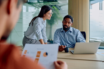 Diverse business people discussing financial charts and using laptop during an important corporate...