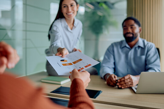 Businesswoman passing financial document with charts and data to coworker during a corporate team meeting in the office - Powered by Adobe