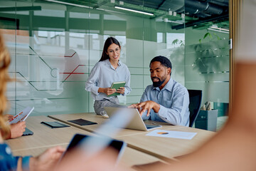 Business professionals discussing work and sharing ideas in a modern glass office. Colleagues planning strategy using technology