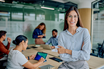 Confident businesswoman with arms crossed smiling at the camera, a diverse team collaborating and working in a modern office