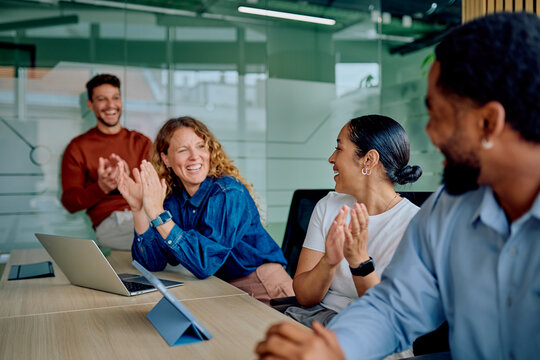 Diverse business professionals in an office meeting room, happily clapping and smiling during a celebration or successful presentation