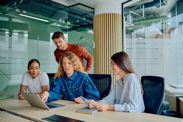 Diverse business colleagues collaborating on a laptop in a modern office, sharing ideas and working...