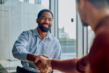 Diverse businessmen shaking hands and smiling during a meeting, celebrating a successful deal and...