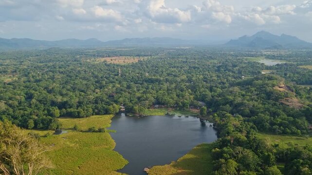 View from Lion Rock across Sri Lanka&rsquo;s scenic heartland, where a calm lake, dense greenery, and forest stretch toward distant mountains beneath a partly clouded sky