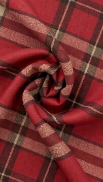 Vertical video: Shifting red plaid rosette reacting to camera jiggle, tightening curl on table