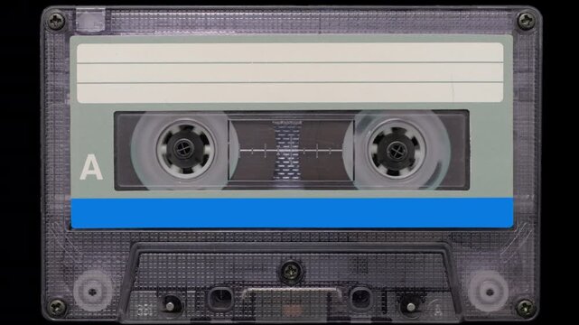 Vintage Audio Cassette Rewind Close-Up. Retro compact cassette tape with spinning reels on black background.	
