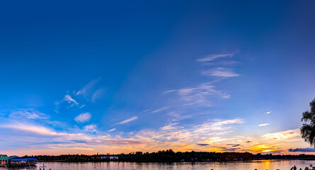 An evening sunset of intermingled cloud patches creates a layered, three-dimensional panoramic picture. The interplay of orange and blue tones. The river reflects the colors of the sky in its waves.