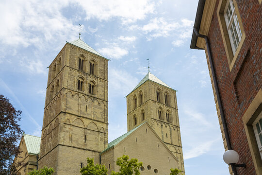 View of the majestic St. Paulus Dom cathedral, its stone towers reaching towards the bright blue sky with scattered clouds, framed by the brick architecture, Muenster, North Rhine-Westphalia, Germany.