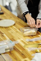 A person seals a container of cake. Several wrapped sweets, cutlery, and an empty plate rest elegantly on the wooden table, inviting a moment of indulgence
