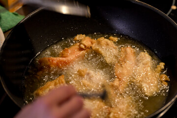 Stirring golden chicken pieces frying in hot oil in a deep pan in the kitchen