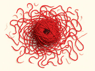 A red yarn ball sits on a light surface, with messy strands spreading out in all directions like a playful tangle