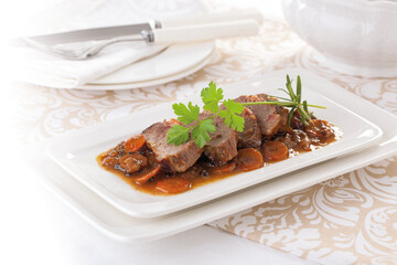 Goose meat stew with black pepper, served on a white platter.