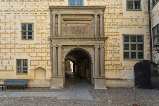 View of an arched stone entrance of Kalmar Castle, framed by decorative brickwork and classical columns, leads into a shadowed passageway, Kalmar, Kalmar County, Sweden.