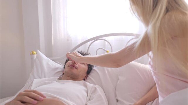 A young woman covering mouth of her husband with hands while her partner snores loudly next to her in bed