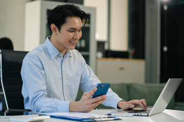 Businessman using laptop computer and smartphone in office. Happy man, entrepreneur, small business owner working online.