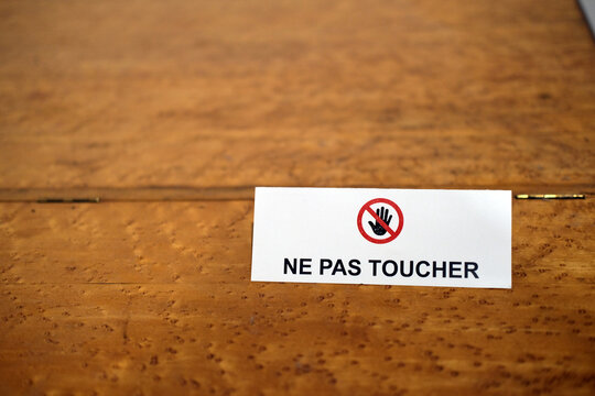 White rectangular sign on wooden surface displaying the French text &ldquo;NE PAS TOUCHER&rdquo; (&ldquo;DO NOT TOUCH") with red prohibition hand symbol.