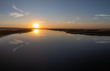 Serene river landscape at sunset with golden sun reflecting on calm water surface