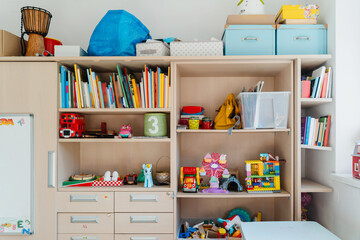Details of interior decor of children's room with cabinet containing shelves of toys. Organizing storage in child's room - shelf with books and toys. Interior of nursery. Montessori education. © nataliaderiabina