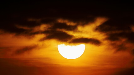 View of the radiant sun partially obscured by dark, brooding clouds, casting a warm glow across the sky in Islamabad, Islamabad Capital Territory, Pakistan.