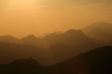 View of hazy, golden sunlight softly illuminating the undulating silhouettes of distant mountain ridges, creating a serene and ethereal landscape, Islamabad, Islamabad Capital Territory, Pakistan.