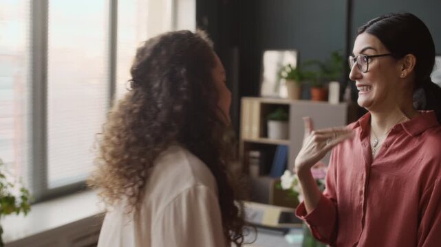 Close up of female Caucasian colleagues smiling, giggling and dossiping while having break during workday in office