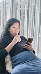 Pregnant Woman Drinking Nutritious Milk While Relaxing and Browsing Her Smartphone