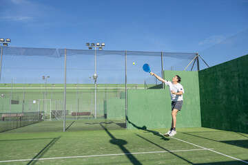Male player serving padel ball on court
