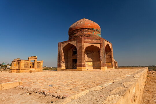 View of ancient brick buildings under a clear blue sky, the warm tones of the structures contrasting with the sky, capturing a moment of history, Thatta, Sindh, Pakistan.