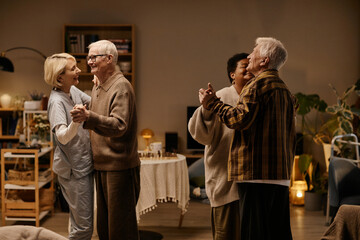 Group of senior men and women dancing together in nursing home, smiling and holding hands, multiethnic seniors enjoying social activity in communal living space