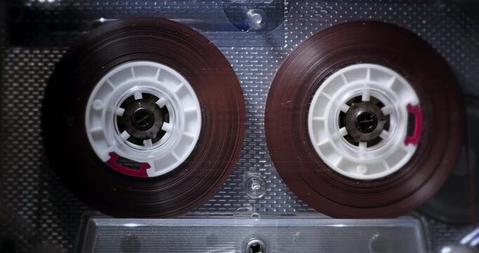Vintage Audio Cassette Reels Spinning. Close-up of retro compact cassette tape with rotating spools inside player.	