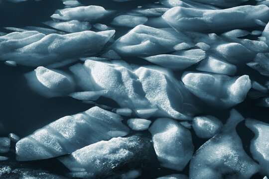 View of fractured ice floes glisten under the cold sun, contrasting with the dark, still waters in Ticino, Bedretto, Ticino, Switzerland.