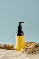 Dark cosmetic pump bottle with a bright yellow label displayed on sand and natural driftwood.