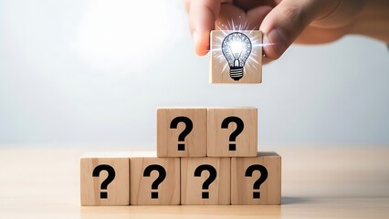 A hand placing a lightbulb on top of a pyramid of wooden blocks with question marks symbolizing a great idea or solution