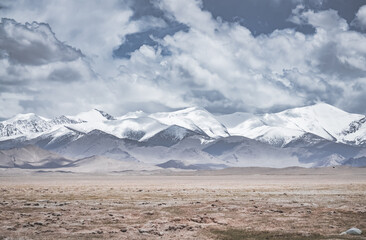 Landscape in the Pamir Mountains of Tajikistan with snow, glaciers, and cliffs, a panorama of mountains in cloudy weather for the background, nature in the Tien Shan highlands, landscape background